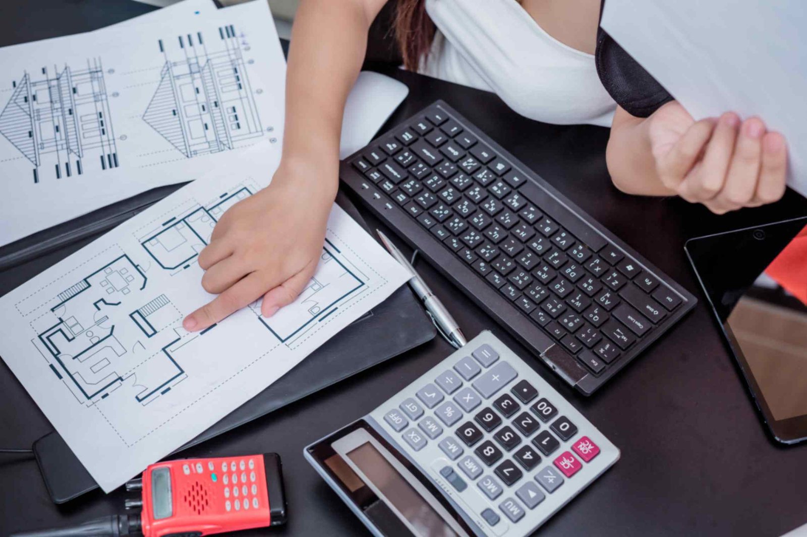 A woman focused on her computer, surrounded by blueprints and a calculator, working on a design project.