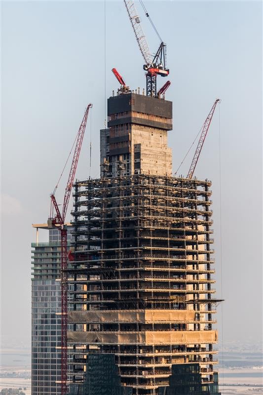 A tall building under construction, surrounded by cranes, showcasing the progress of urban development.